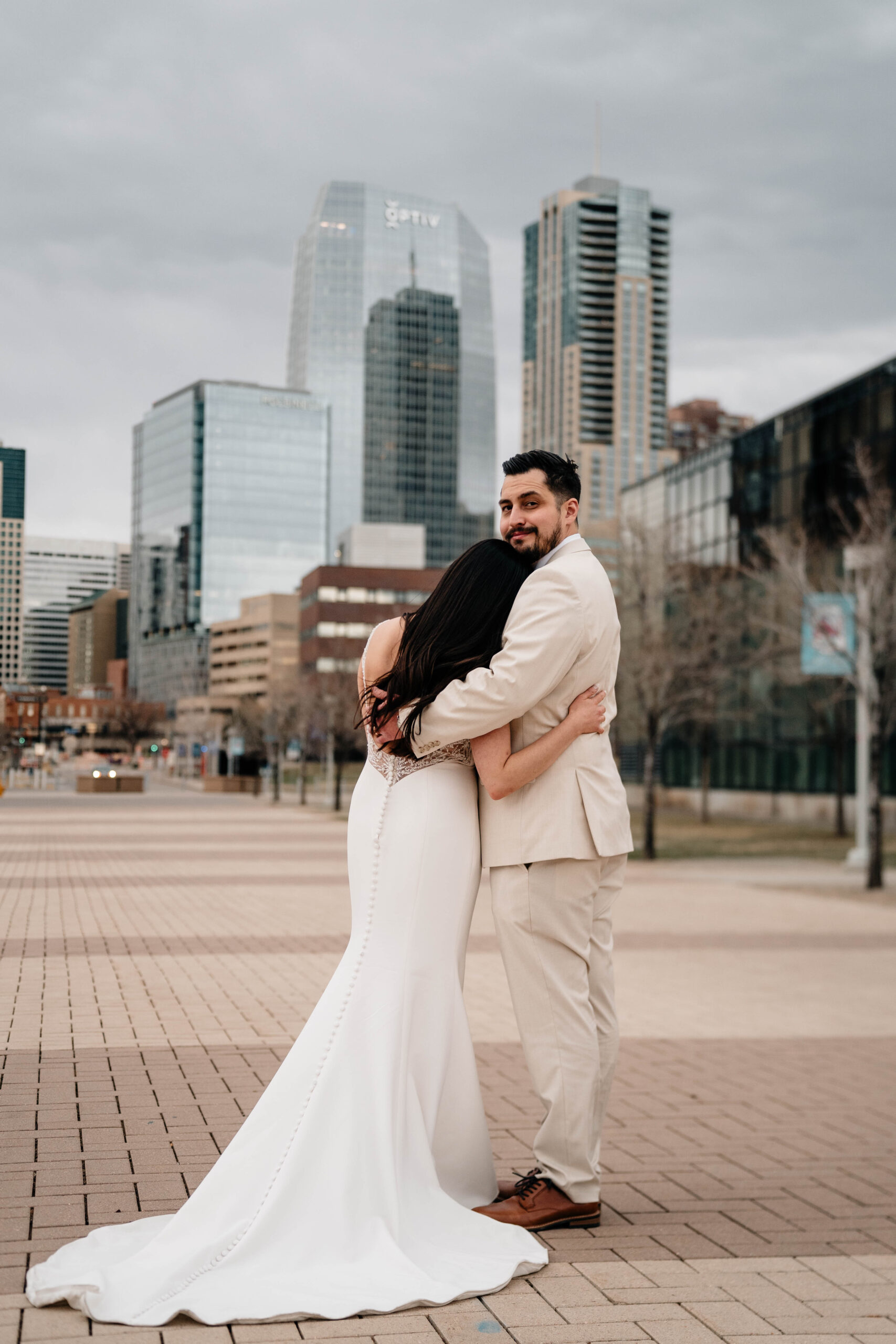 Bride and Groom hug in front of Denver skyline. 
